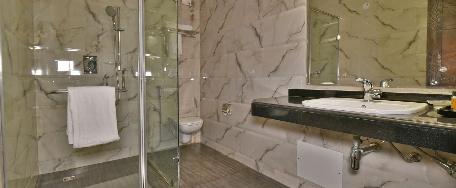 A shower cubicle with a wash basin beside it, featuring toiletries placed on the counter at DLS Hillcrest Resort, Shimla.